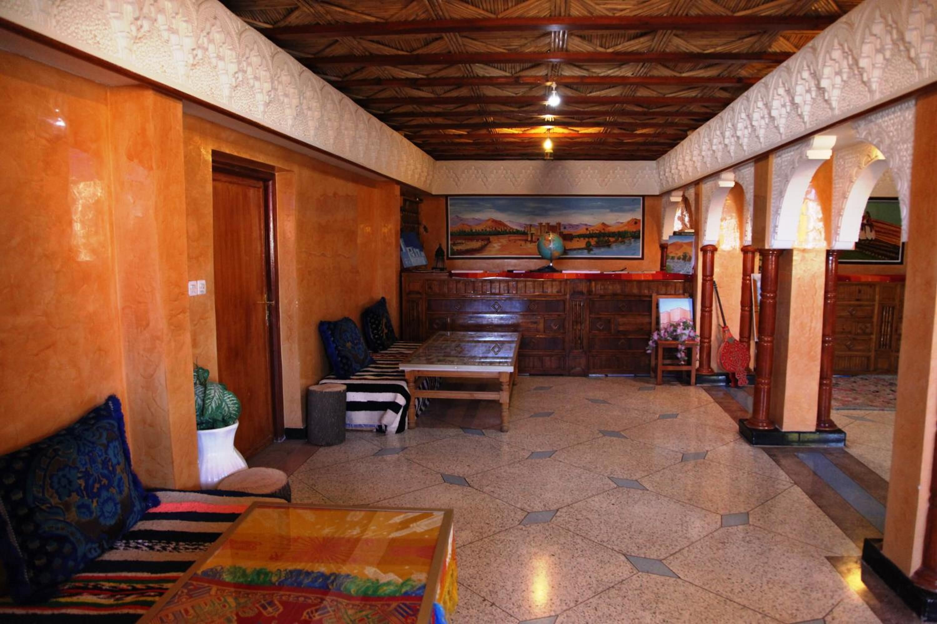 A lobby with a wooden ceiling, a painting on the wall, a reception desk, and a seating area with a colorful rug.