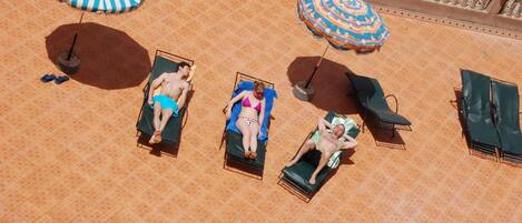 Vista aérea de un área de piscina con azulejos, sillas de descanso y sombrillas.