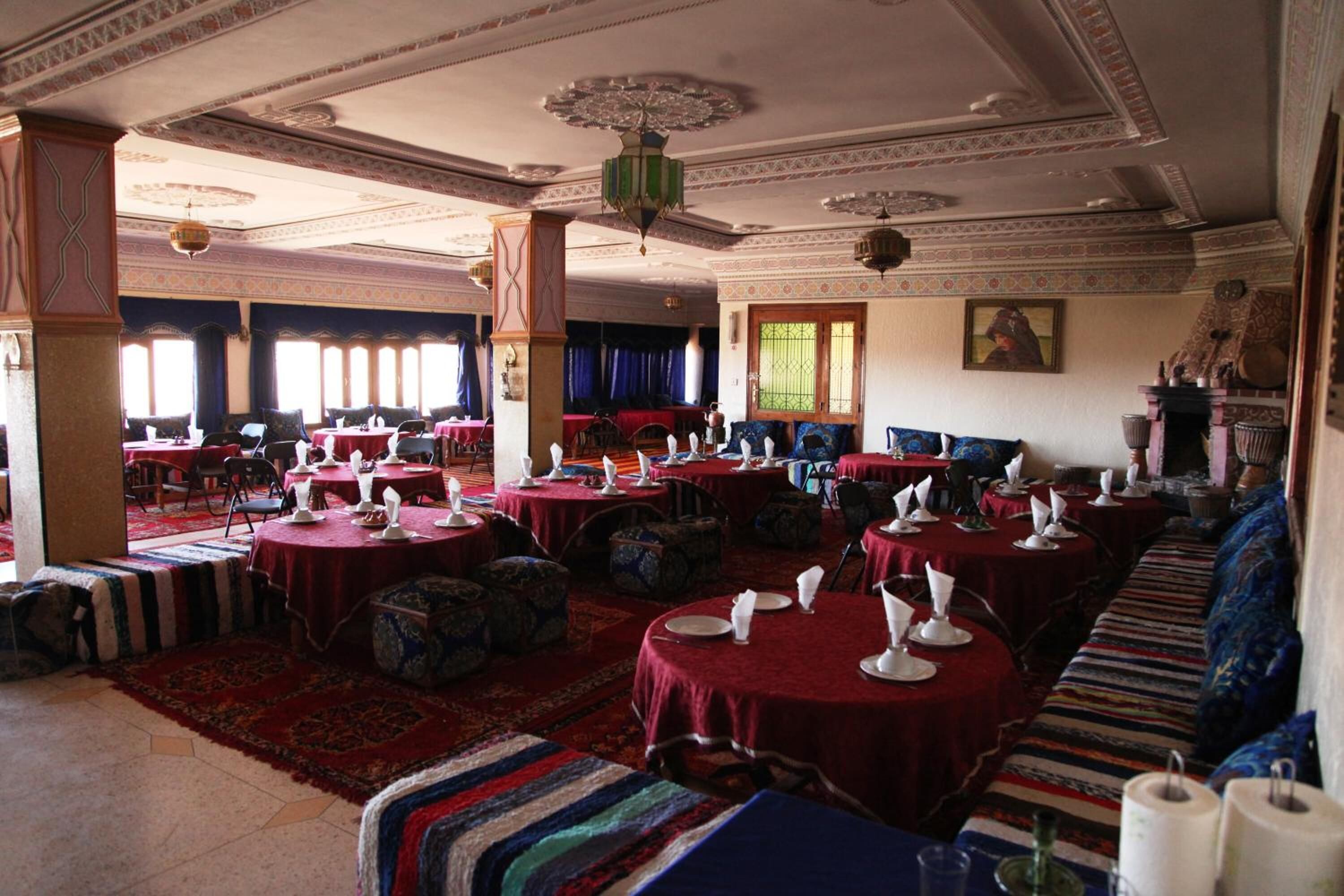 A spacious dining hall with round tables set for meals, featuring traditional decor and a large sofa area.
