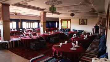A spacious dining hall with round tables set for meals, featuring traditional decor and a large sofa area.