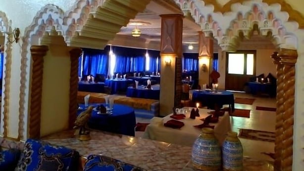 A restaurant with traditional arches, tables set with blue tablecloths, and a decorative bird statue. - La Kasbah De Dades (Boumalne Dades)