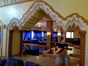 Un restaurante con arcos tradicionales, mesas dispuestas con manteles azules y una estatua decorativa de un pájaro.