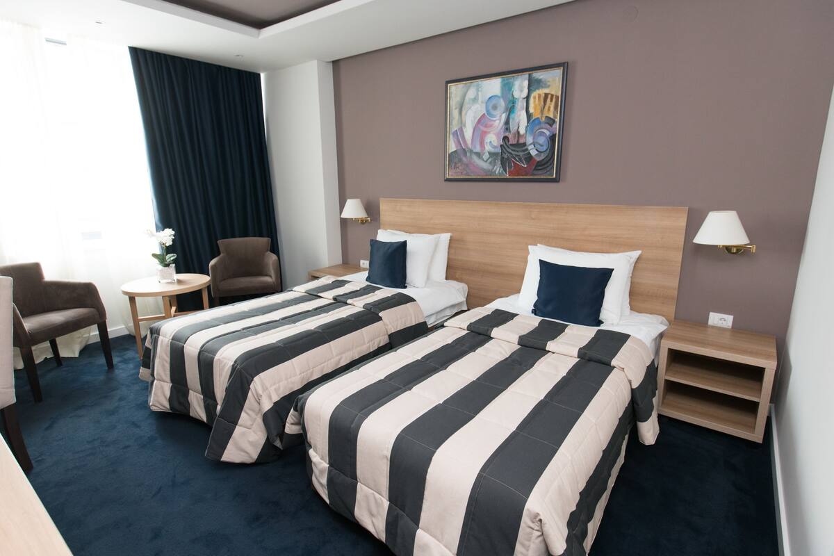 Ein Hotelzimmer mit zwei Betten, einem Sessel, einem kleinen Tisch und einem Bild an der Wand.