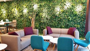 Een gezellige zithoek met banken en fauteuils, een bijzettafeltje en een wand vol begroeiing.