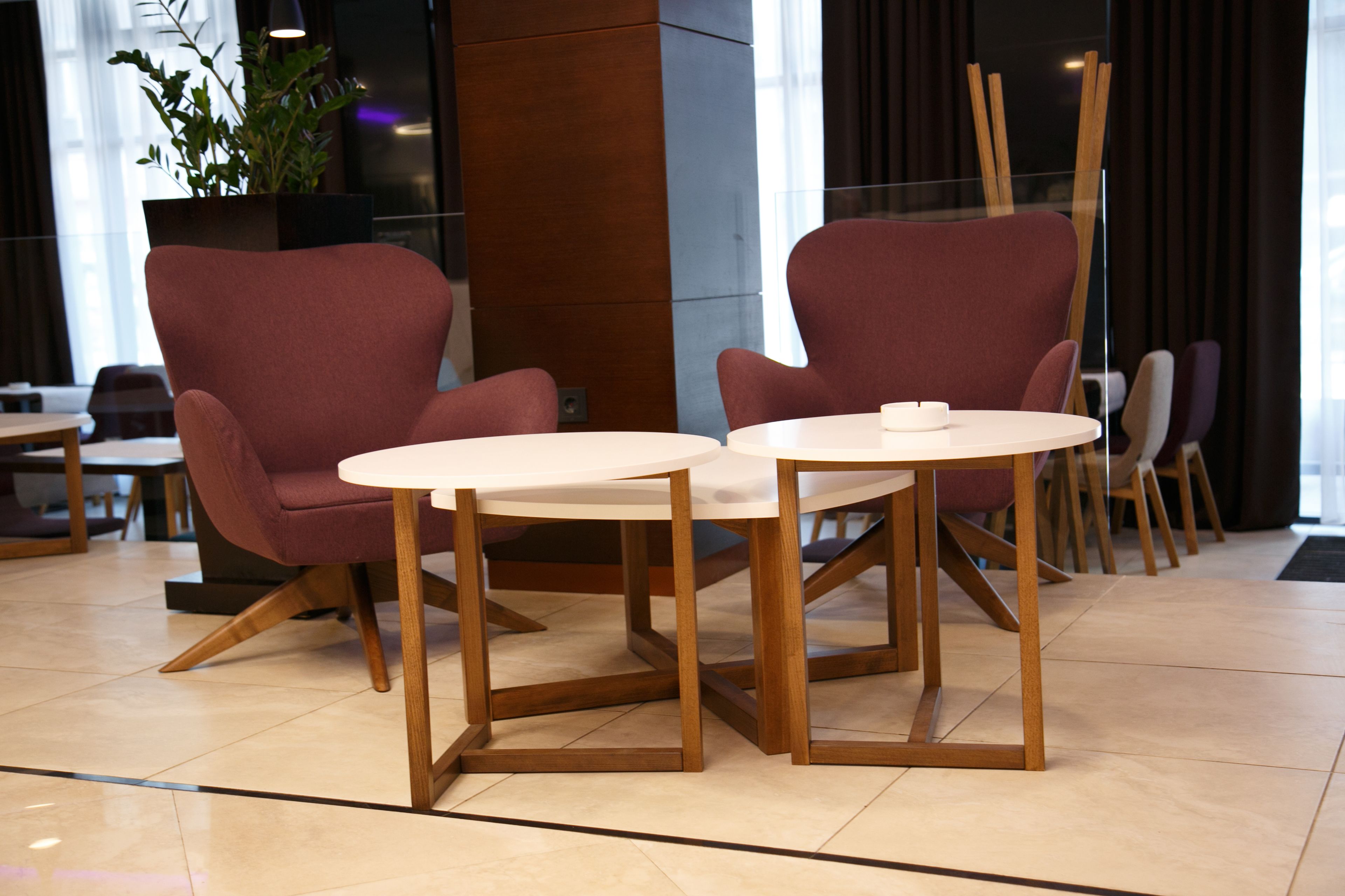 A modern interior with two round tables and matching chairs, a large potted plant, and a wooden pillar.