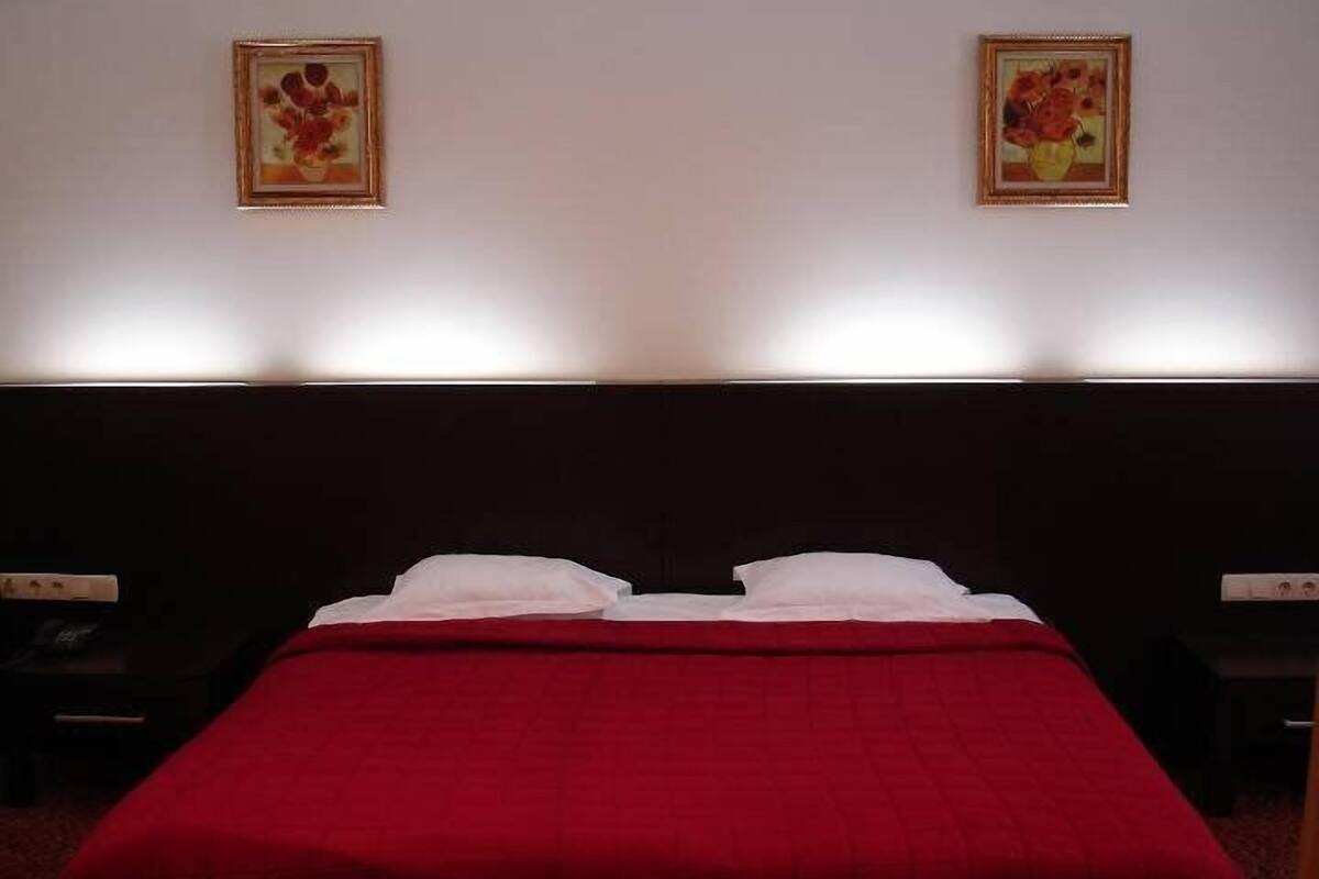 A hotel room with a large bed, two bedside tables, and two framed floral paintings on the wall.