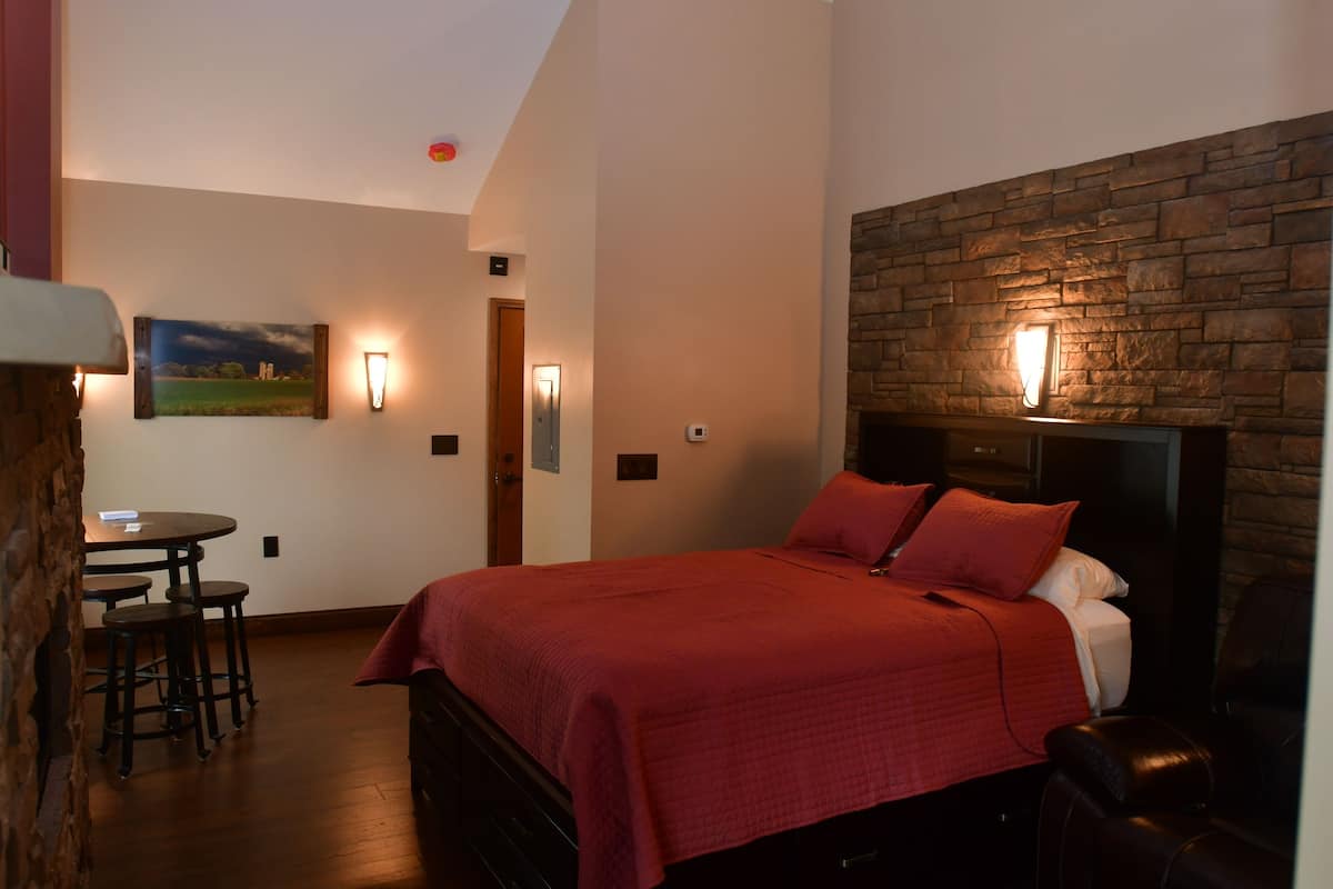 A bedroom with a large bed, a stone accent wall, a dining area with stools, and a painting on the wall.