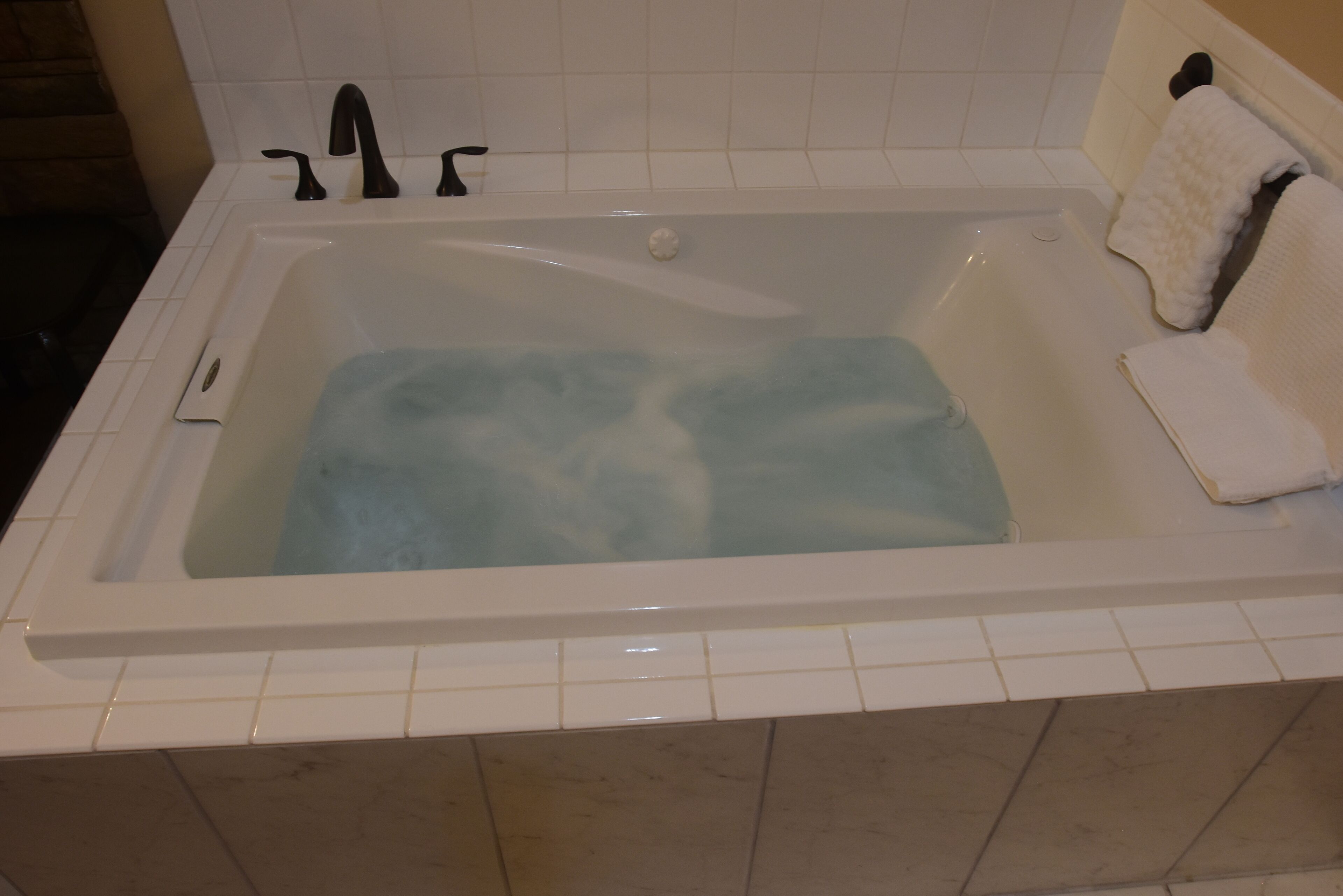Una vasca da bagno bianca con un rubinetto, un asciugamano bianco e un tappetino da bagno bianco.