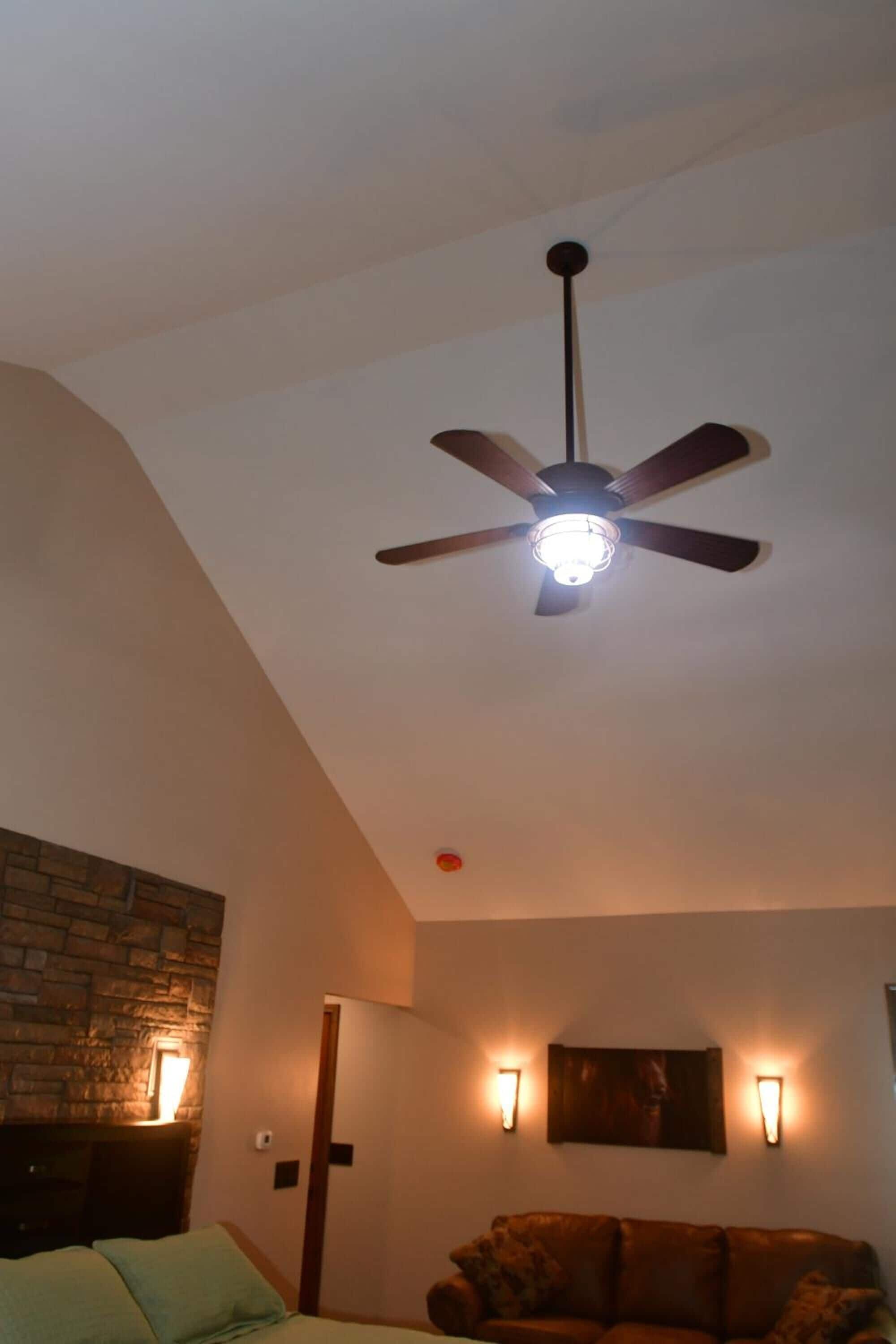 Une pièce dotée d’un ventilateur de plafond, d’un mur en pierre, d’un canapé et de luminaires fixés au mur.