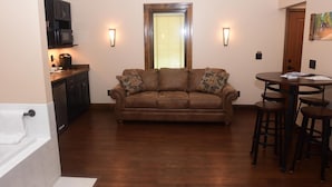 A living room with a brown sofa, a kitchen area with a microwave, and a dining table with stools. - The Fields of Eden Inn (Eden)