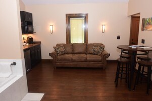 Una sala de estar con un sofá marrón, una zona de cocina con microondas y una mesa de comedor con taburetes.