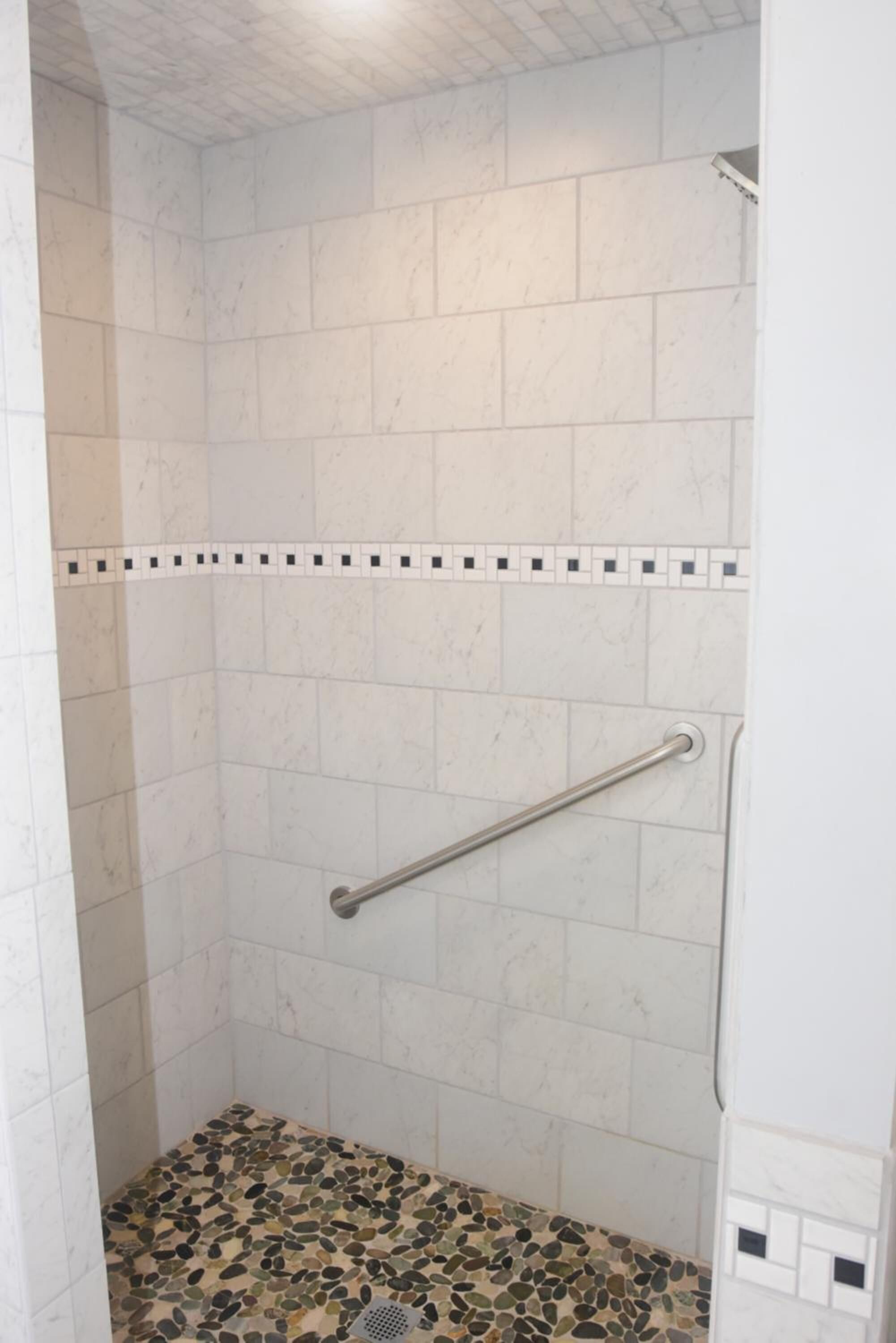 A shower with white tiles and a pebble-patterned floor.