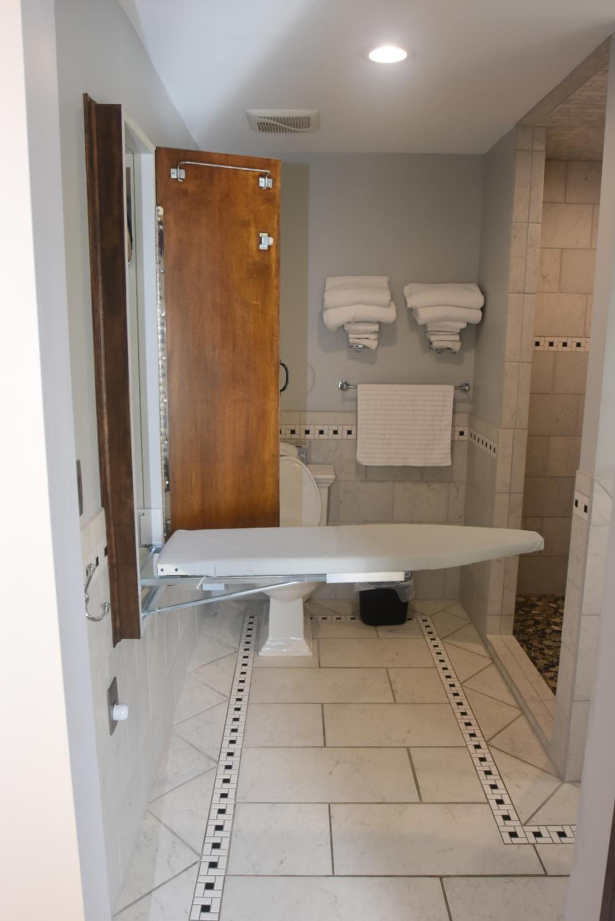A bathroom with a wooden door, a white bathtub, two white towels on hooks, and a shower area with tiled walls.