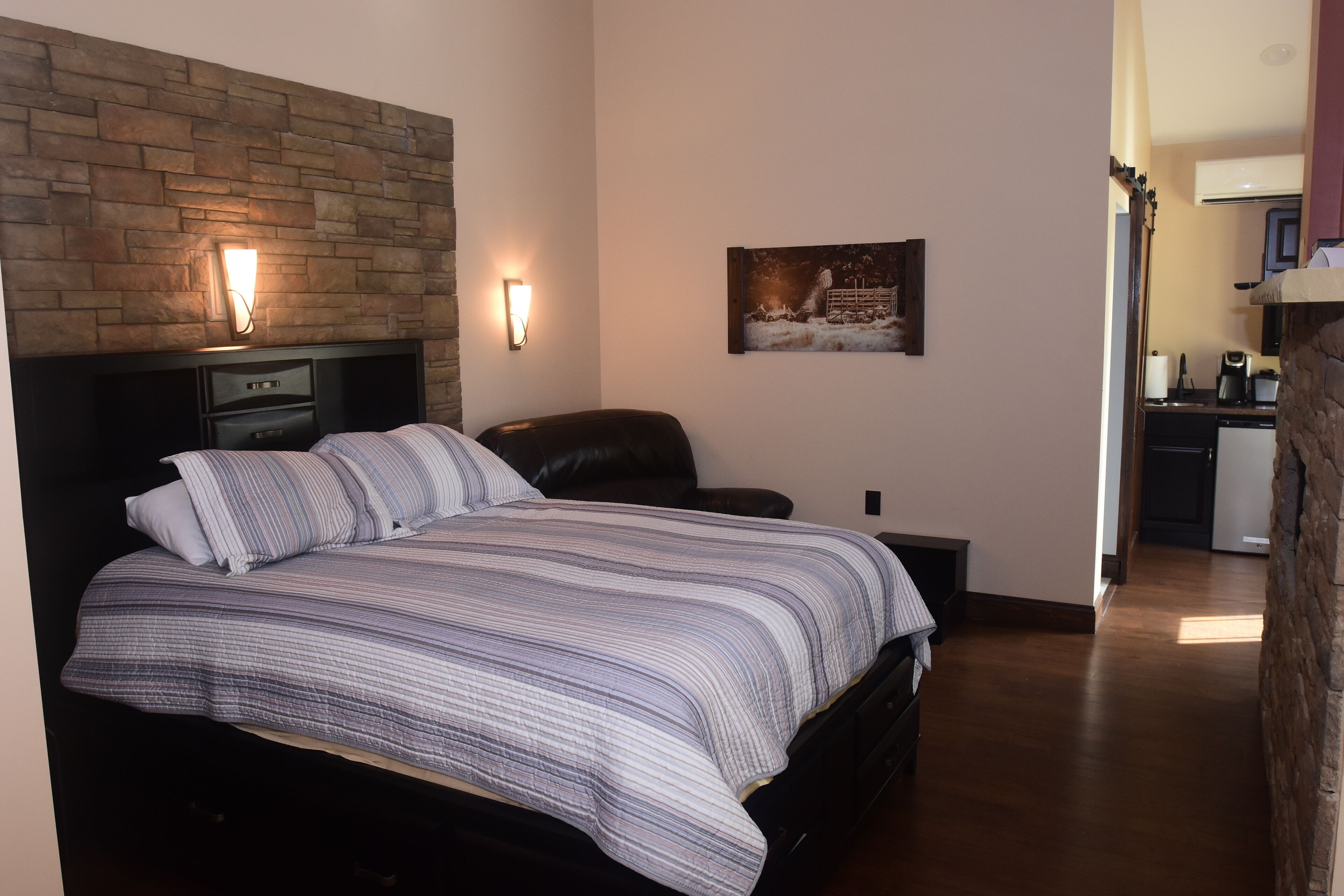 A bedroom with a bed, a nightstand, a chair, a wall-mounted light, and a painting.