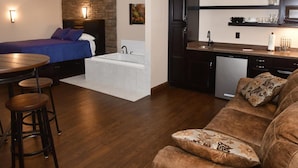 A compact hotel room with a bed, a small kitchenette, a dining area with a table and stools, and a living area with a sofa. - The Fields of Eden Inn (Eden)