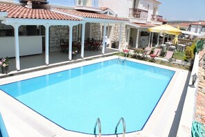 A swimming pool with a white pool deck, a covered patio area with outdoor seating, and a view of the surrounding buildings. - Alacati Lucky Angel Hotel (Cesme)