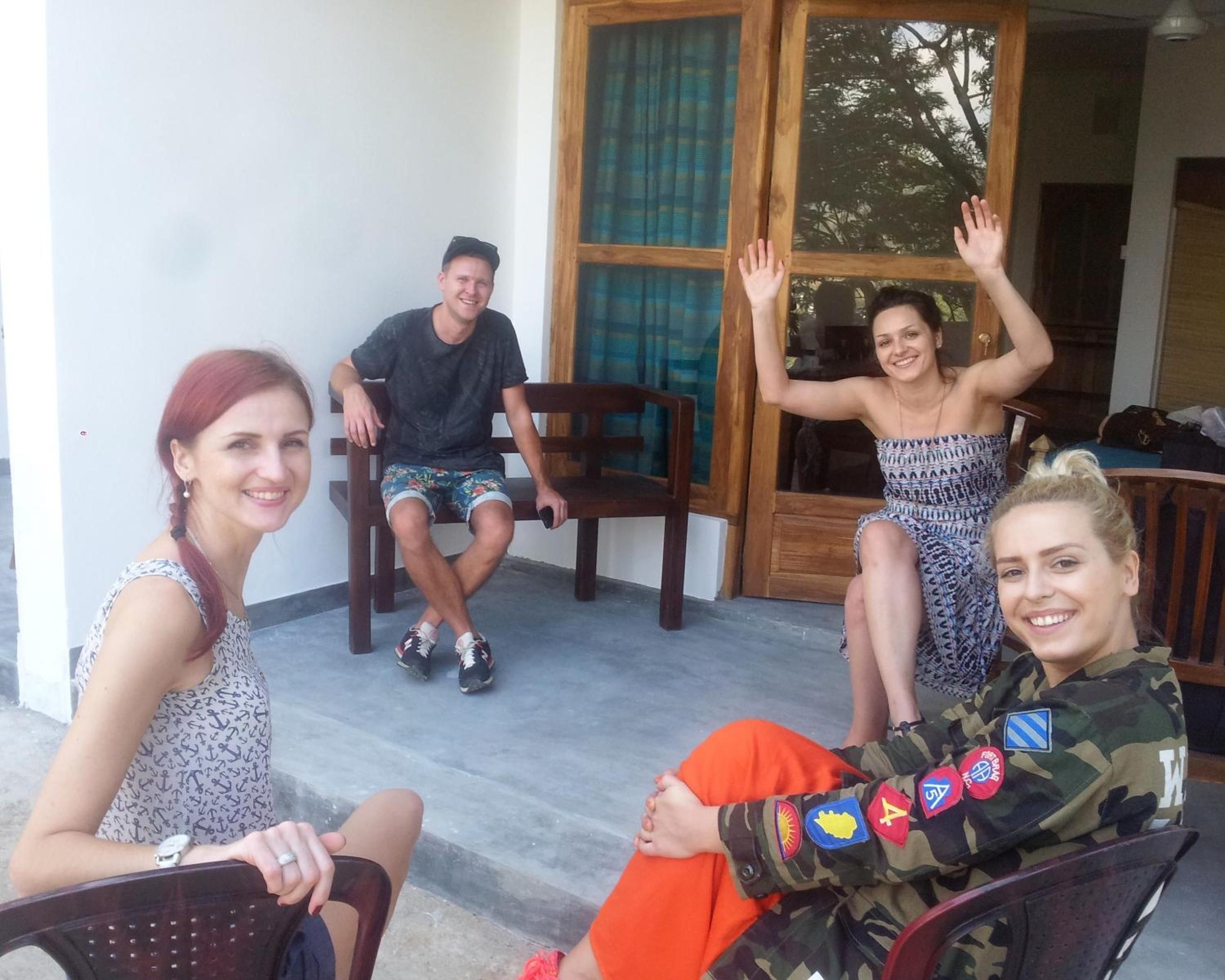 Un grupo de personas sentadas en sillas frente a un edificio con puerta y ventanas de madera.