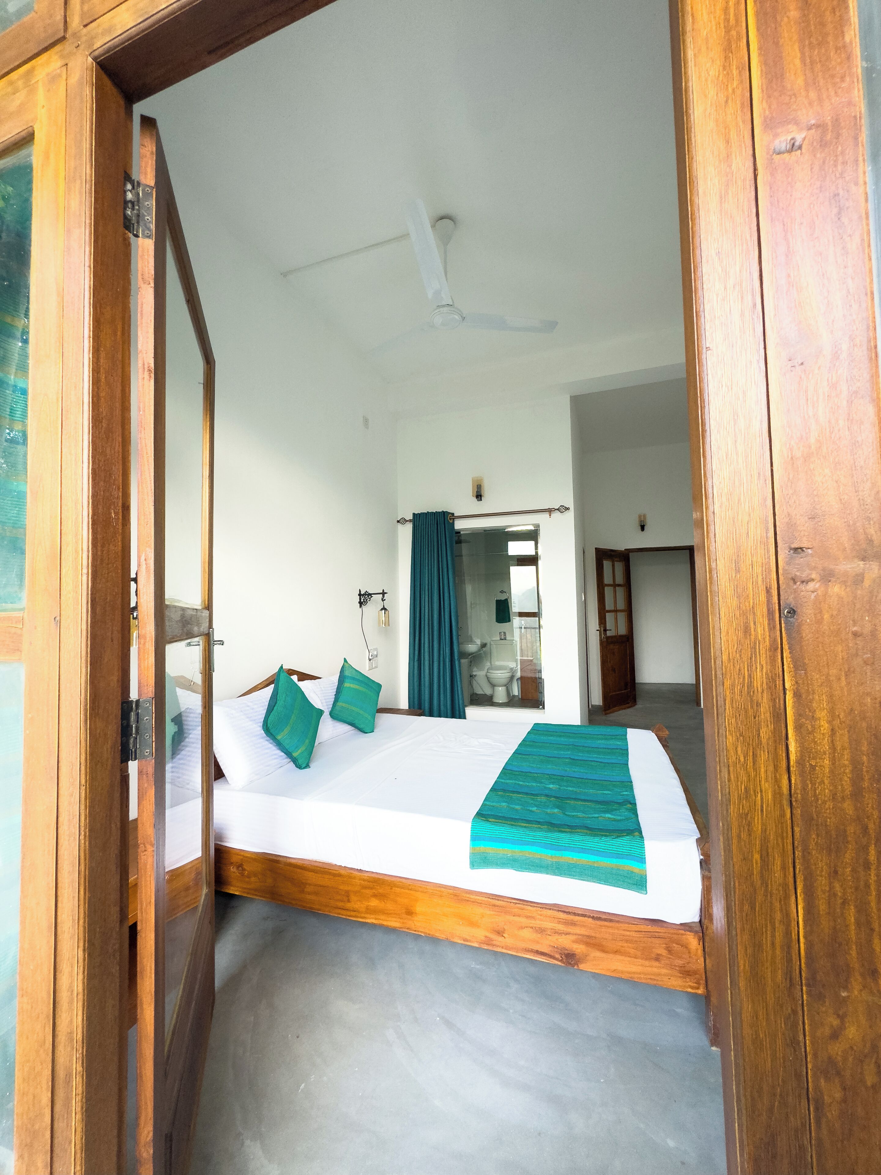 A room with a bed, a ceiling fan, and a bathroom visible through a glass door.