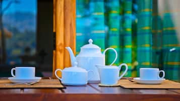 A tea set on a wooden table with a view of green curtains and a window in the background.