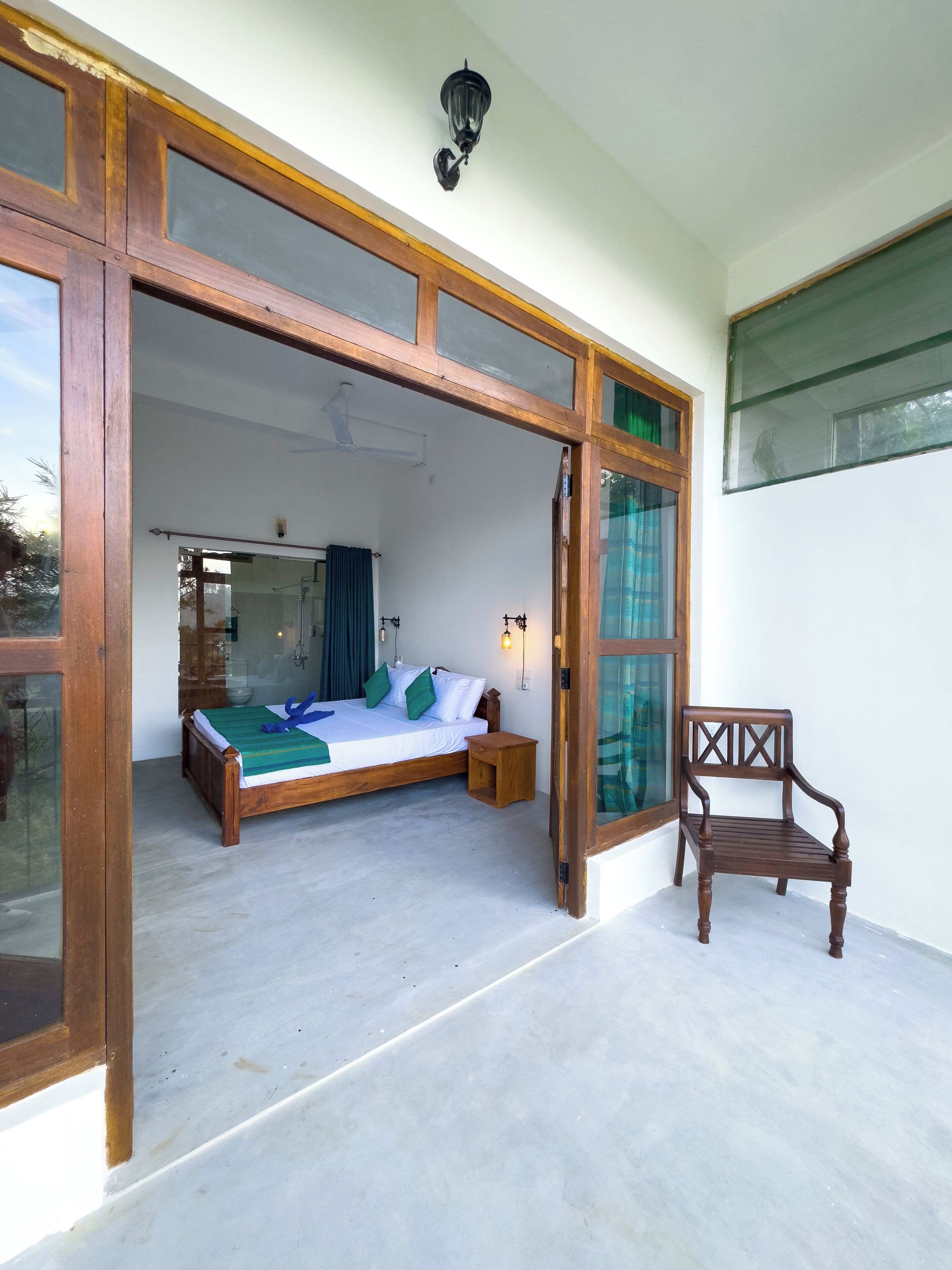 A bedroom with a bed, a wooden chair, and a large glass door leading to another room.