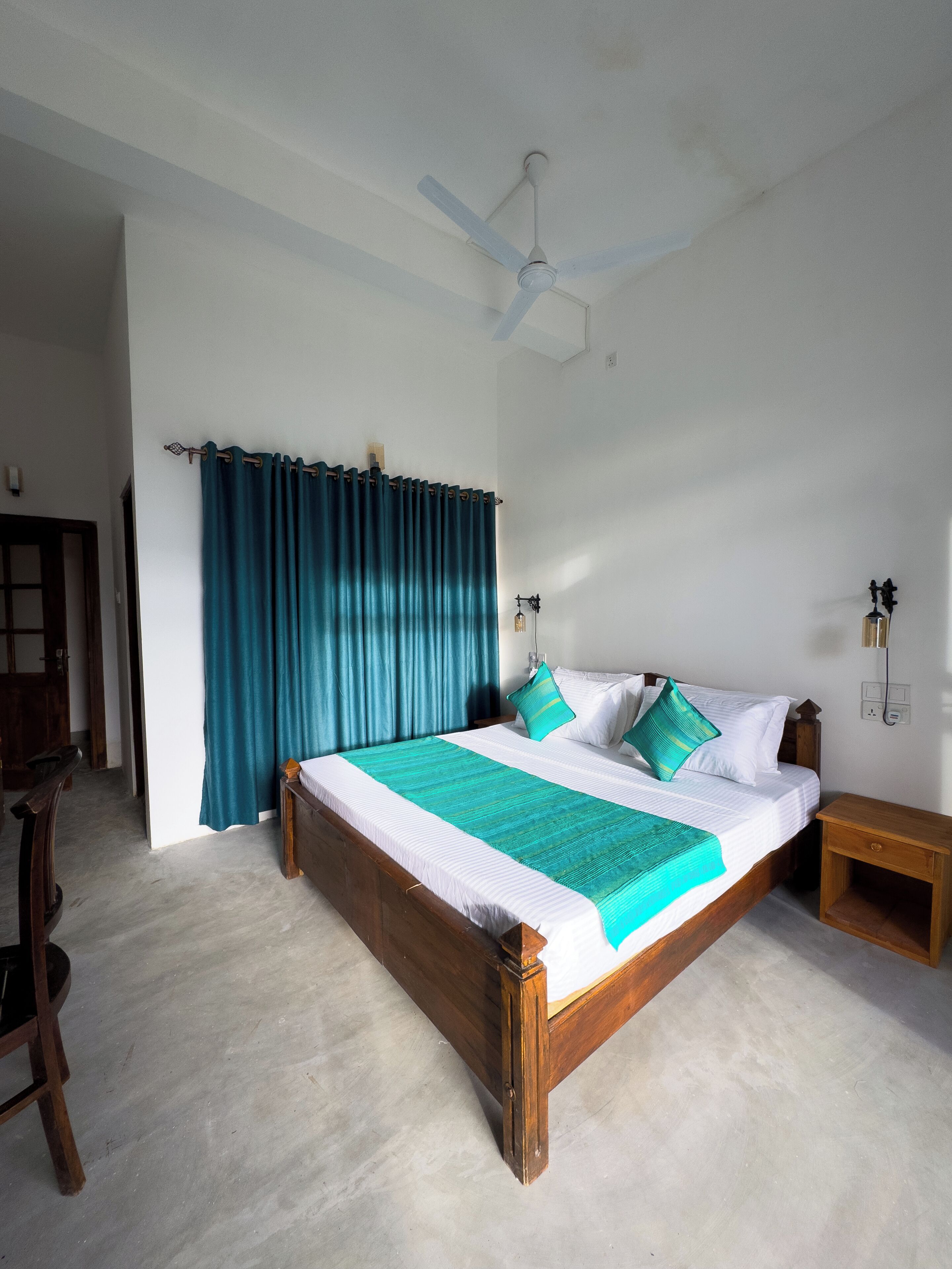 A bedroom with a large bed, a ceiling fan, a wooden nightstand, and a desk with a chair.