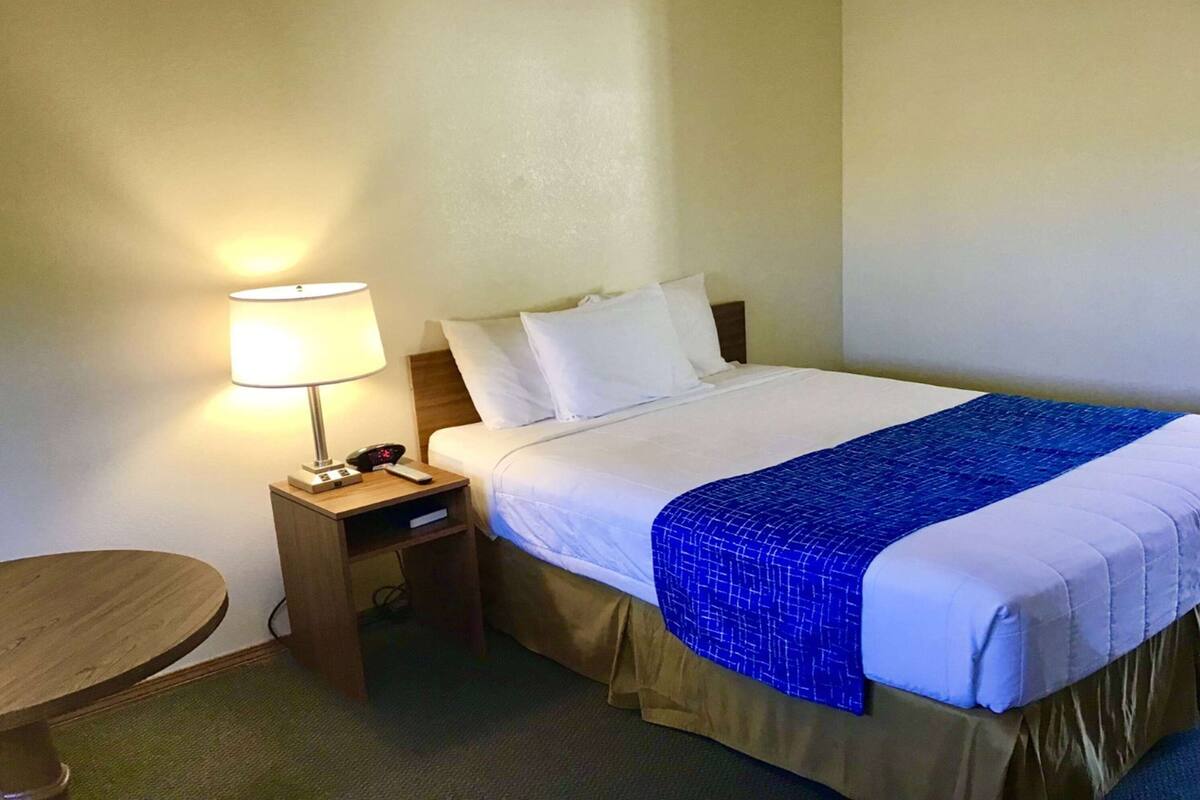 A hotel room with a bed, a bedside table with a lamp, and a small round table.