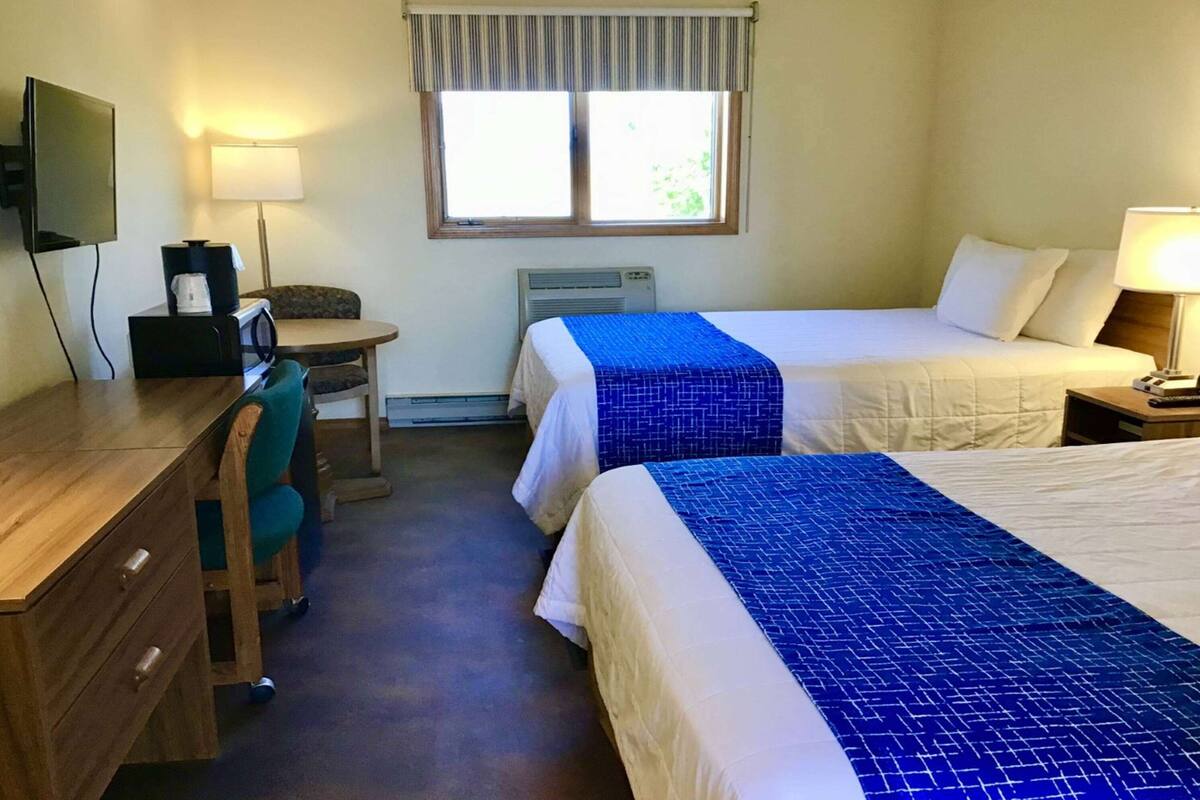 A hotel room with two beds, a desk, a chair, a television, and a window with curtains.