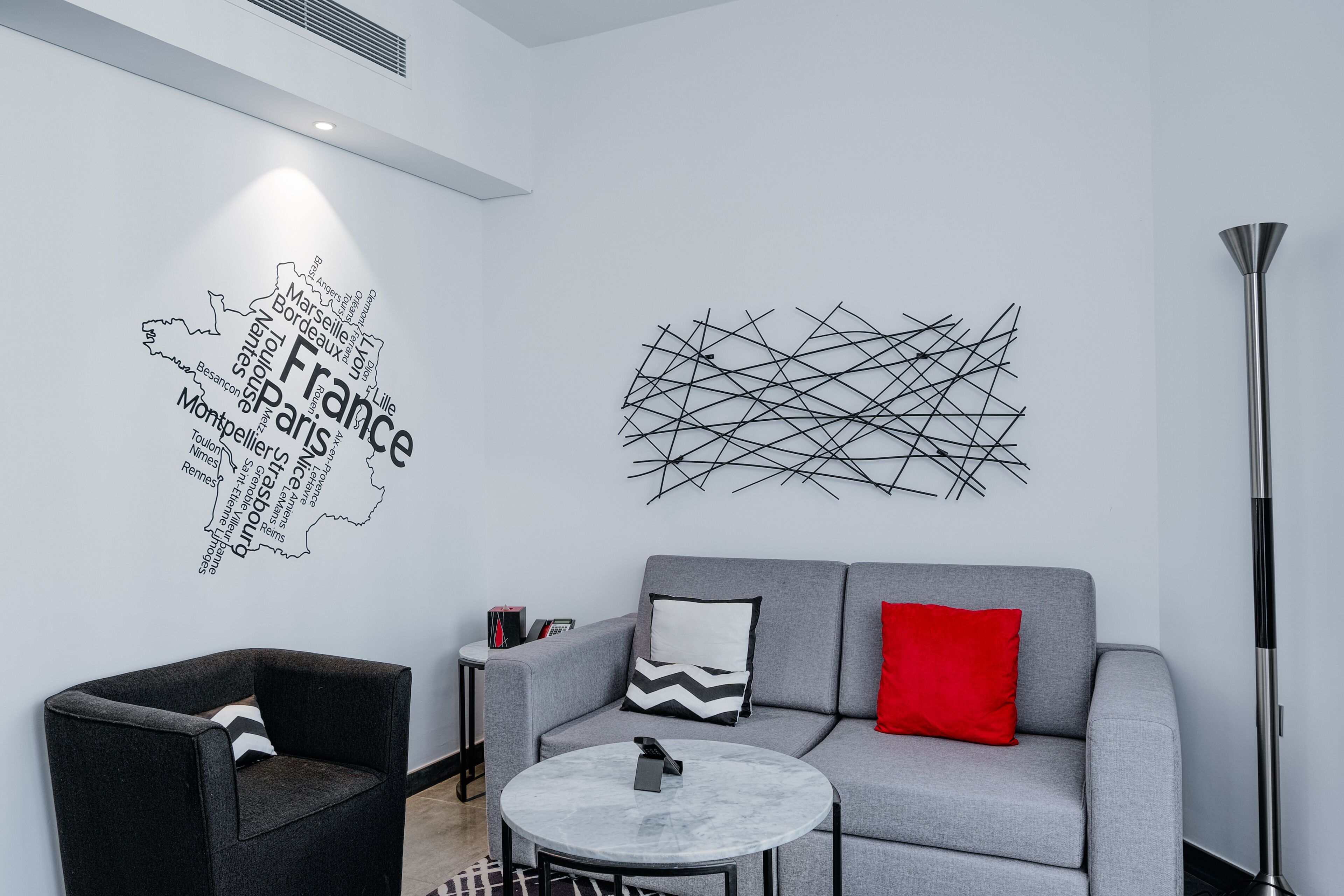 A modern living room with a grey sofa, a black armchair, a round coffee table, and a wall art piece depicting France.