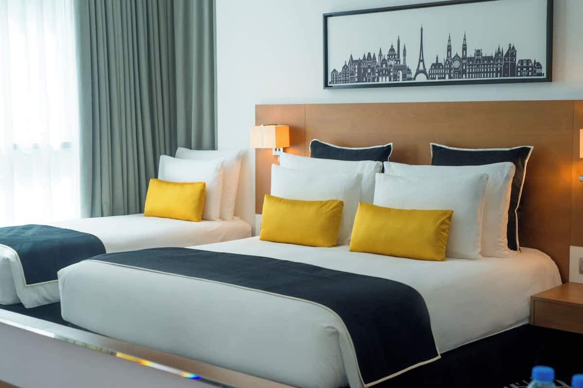 A hotel room with a large bed, two bedside tables, a cityscape artwork on the wall, and a window with curtains.