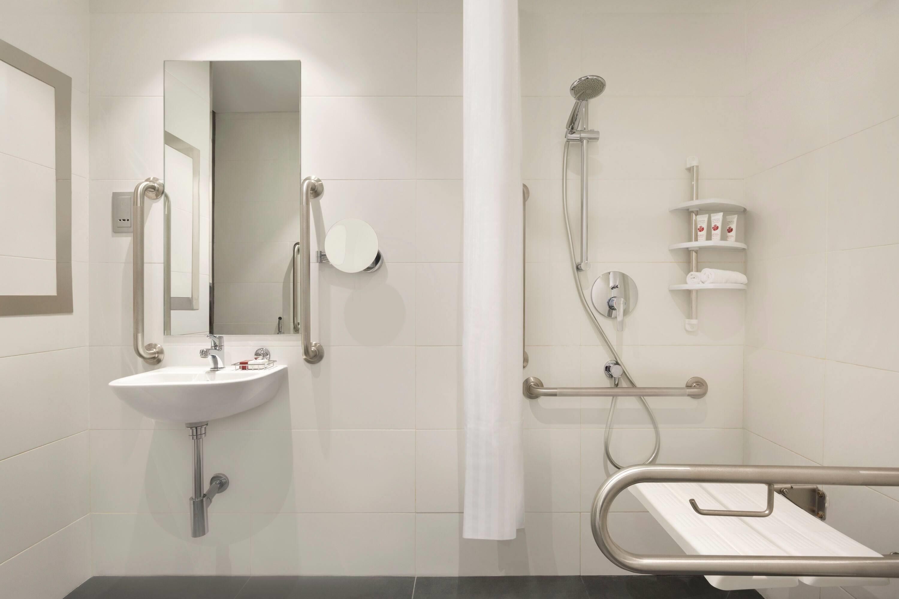 A bathroom with a sink, mirror, shower, and a grab bar.