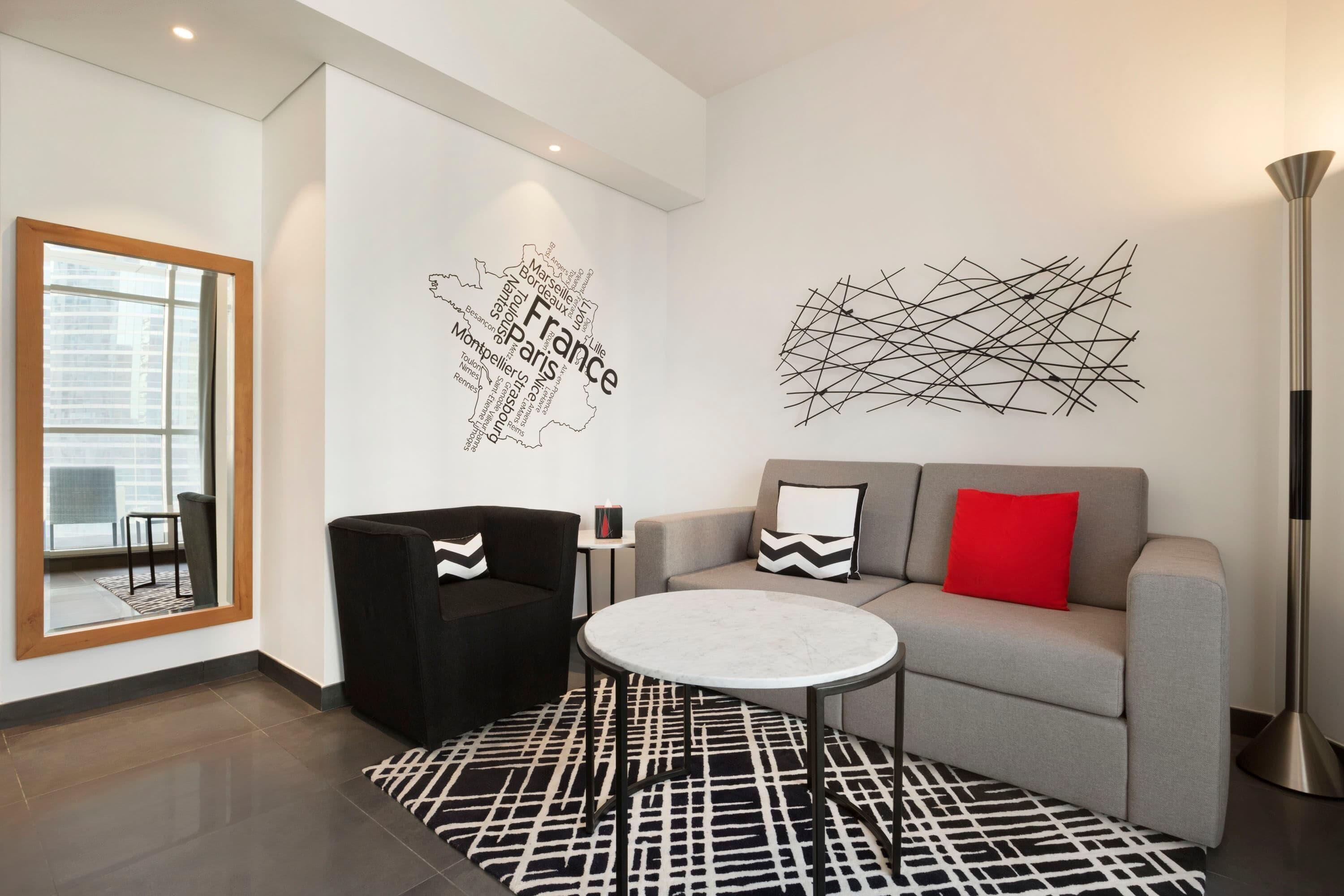 A modern living room with a sofa, a round table, a black and white patterned rug, a wall map of France, and abstract art.