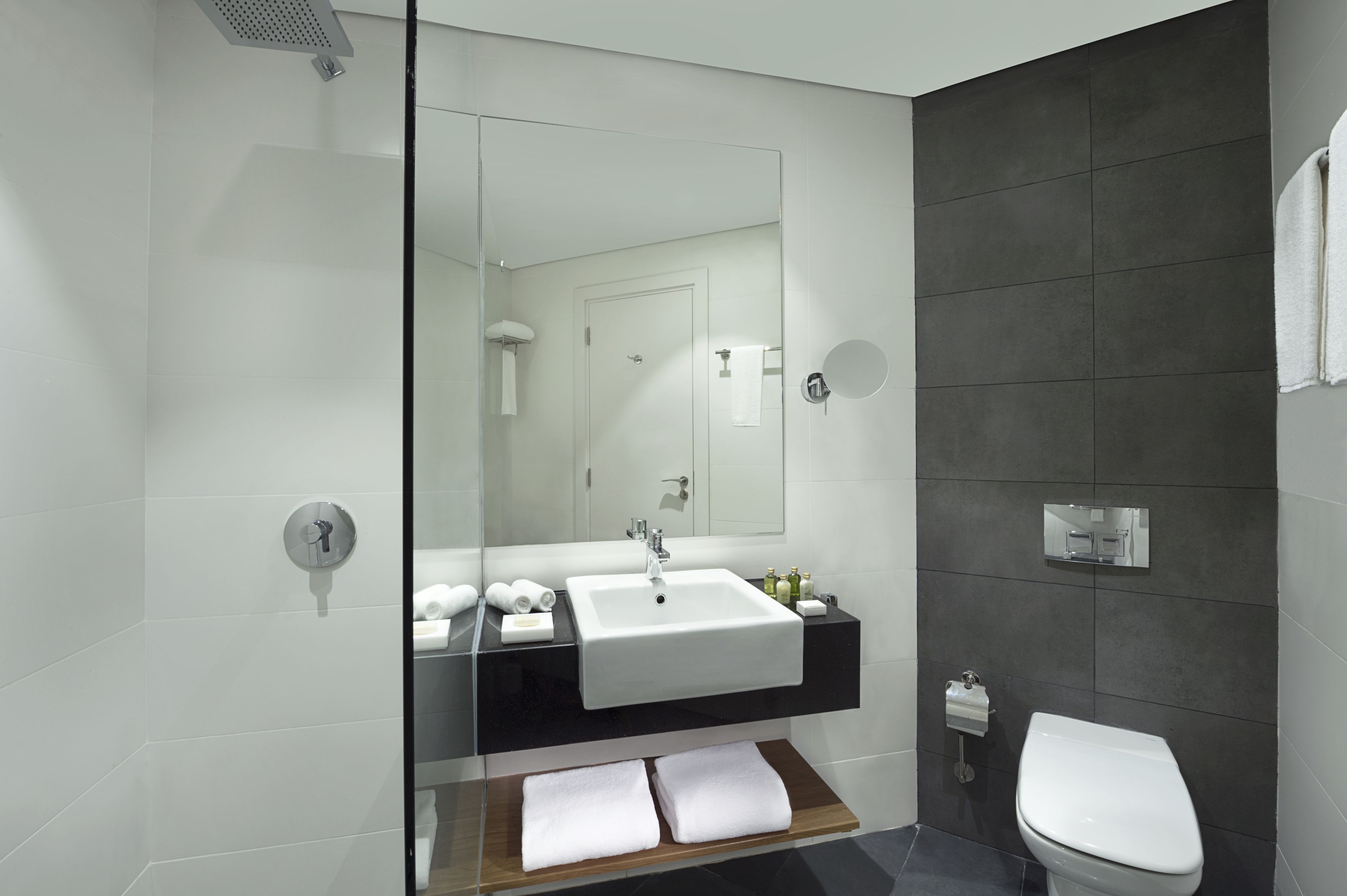 A modern bathroom with a glass shower enclosure, a white sink, and a dark tiled wall.