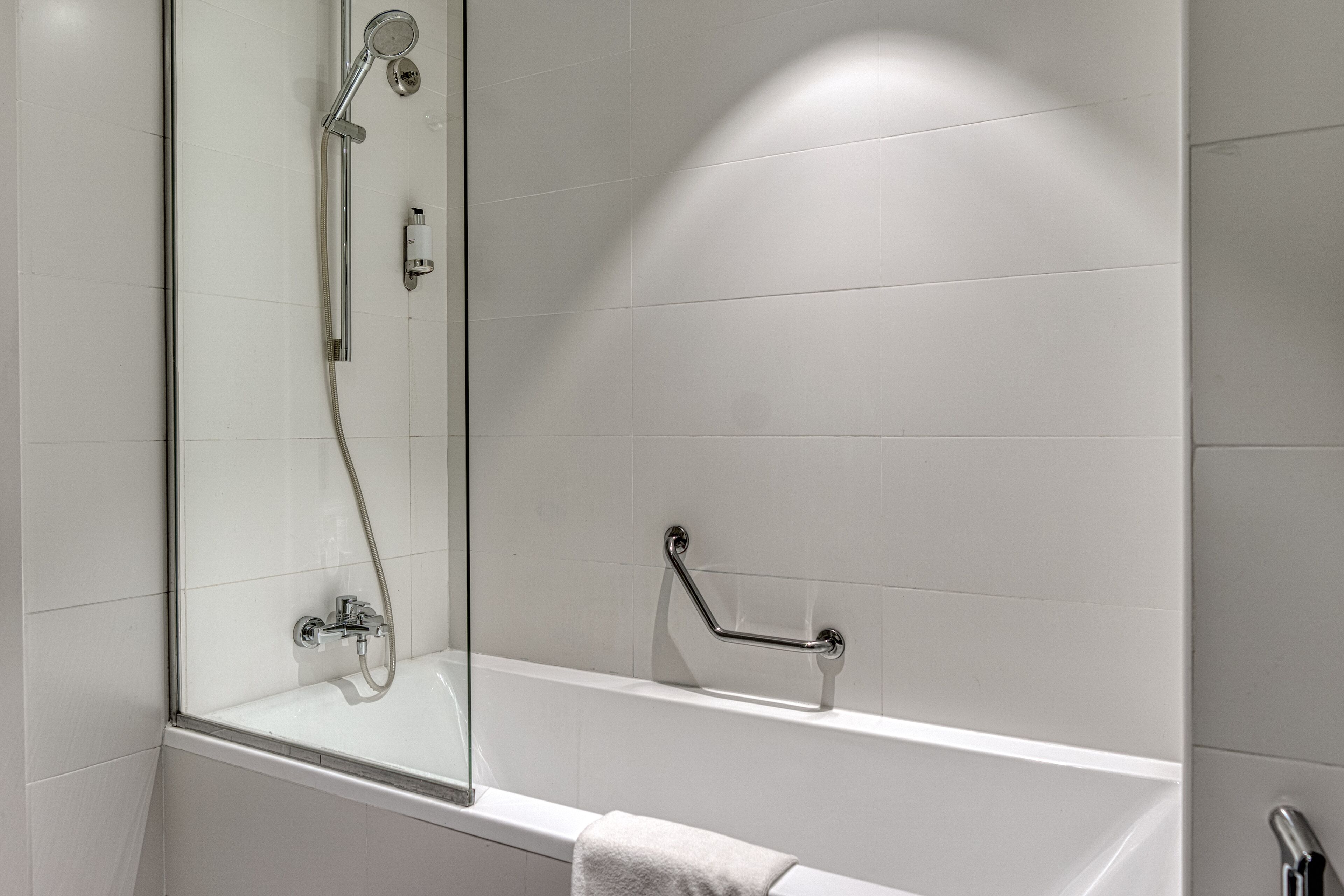 A modern bathroom with a glass-enclosed shower, a white bathtub, and a grab bar for safety.