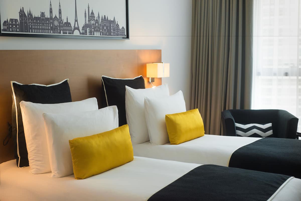 A hotel room with a large bed, two pillows, a nightstand, and a lamp.