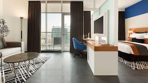Habitación de hotel moderna con un ventanal grande, un escritorio, una silla, una cama y un televisor.