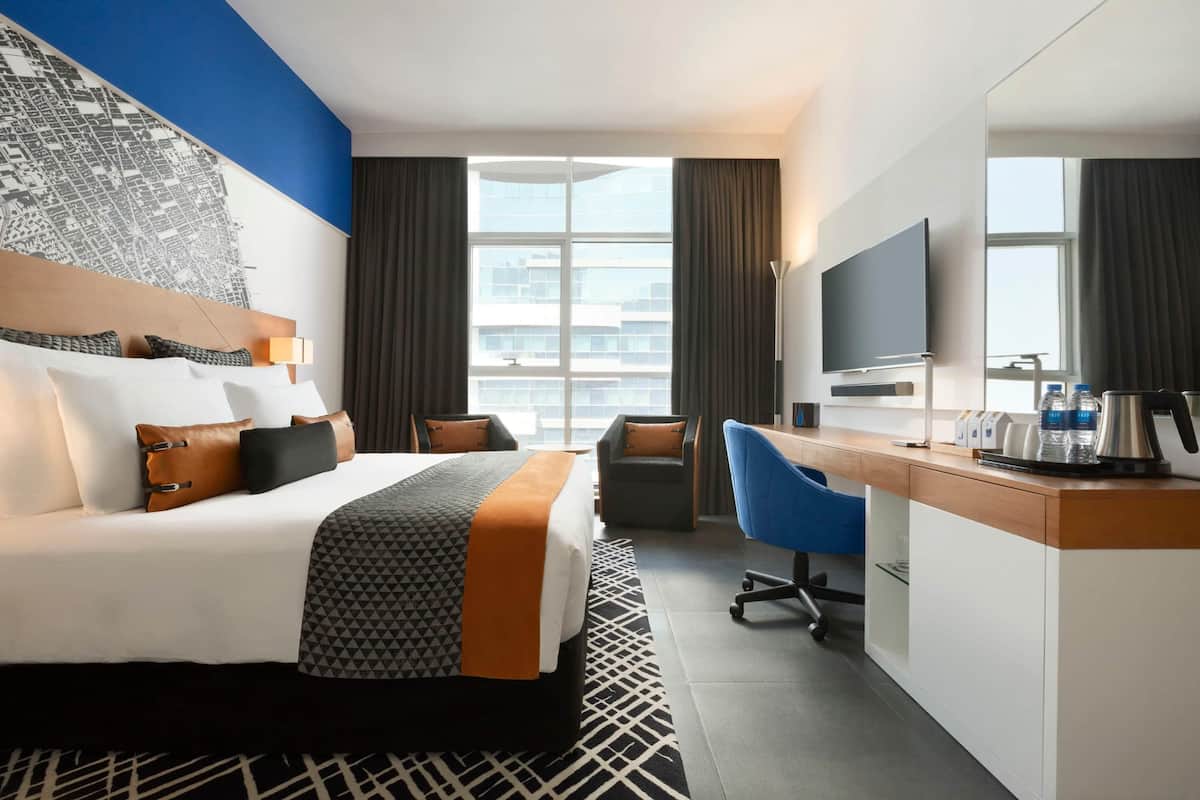 A hotel room with a bed, desk, chair, TV, and a large window.