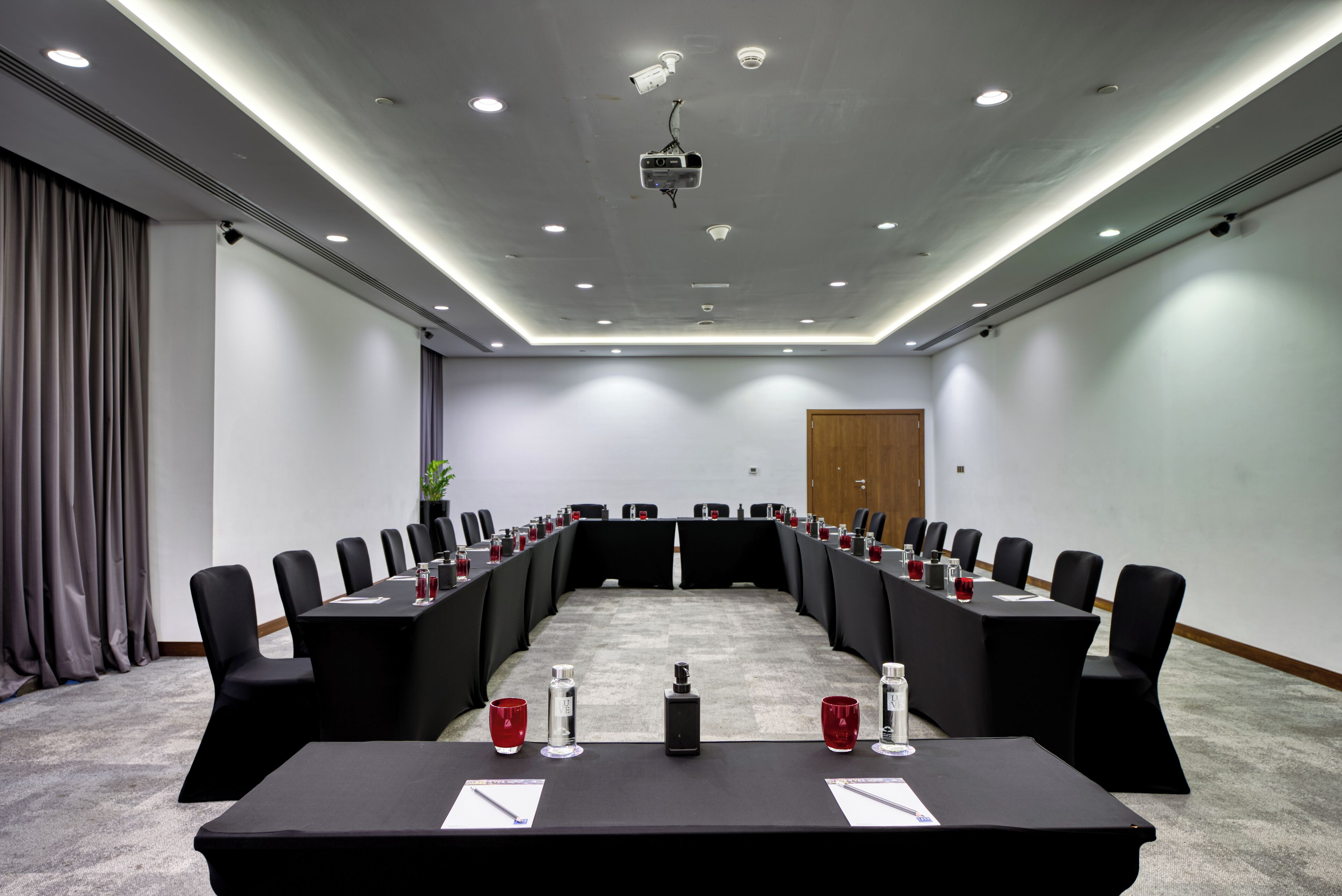 A conference room with a long table, black chairs, and a projector on the ceiling.