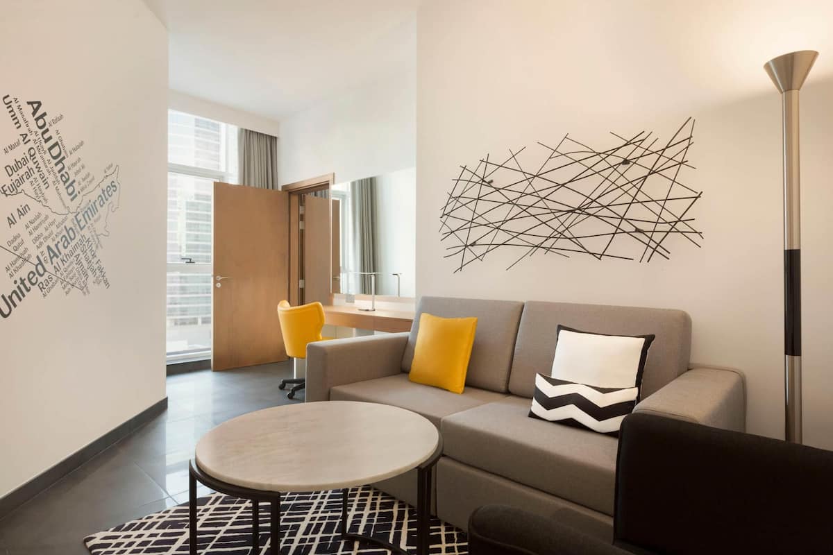 A modern living room with a sofa, two yellow chairs, a round coffee table, and a decorative wall piece.