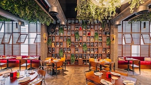 A restaurant with wooden tables and chairs, a large bookshelf filled with books and bottles, and red cushioned seating. - TRYP by Wyndham Dubai (Dubai)