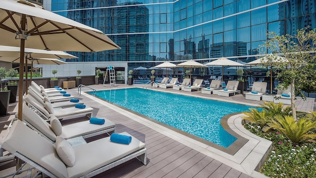 A rooftop pool with lounge chairs and umbrellas, surrounded by a modern building with reflective glass windows. - TRYP by Wyndham Dubai (Dubai)