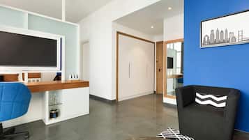 A modern hotel lobby with a reception desk, a blue wall with a cityscape mural, a black armchair, and a patterned rug.