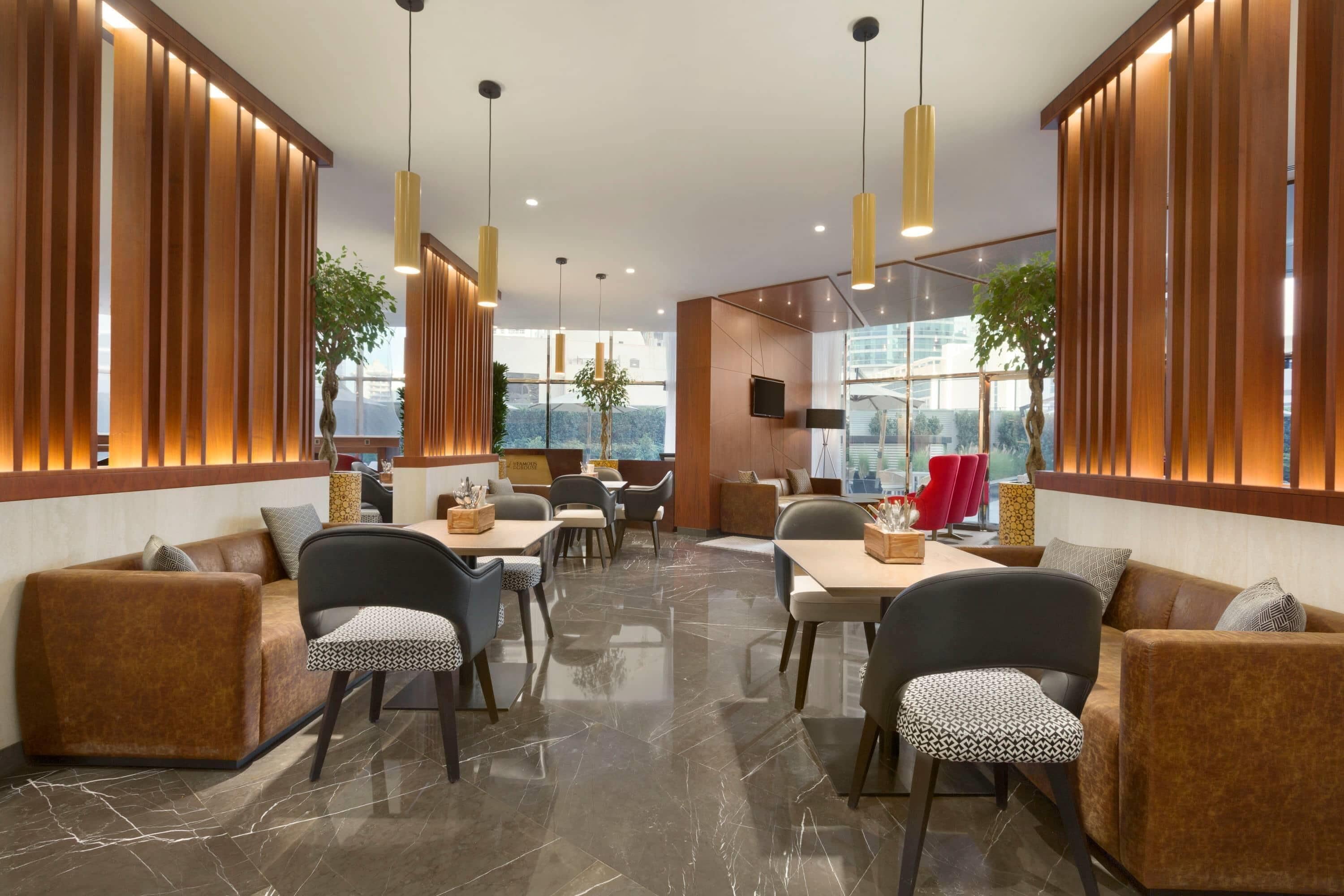 A modern interior with wooden paneling, a dining area with tables and chairs, and large windows providing natural light.