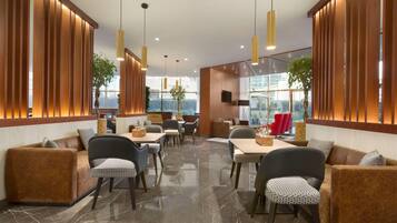 A modern interior with wooden paneling, a dining area with tables and chairs, and large windows providing natural light.