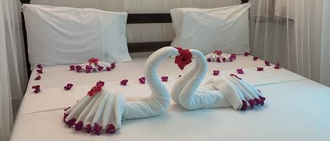 A bed with a canopy, white bedding, and swan-shaped towels.