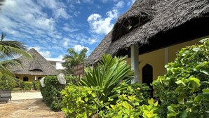 A pathway leading to a building with a thatched roof, surrounded by lush greenery and stone paving. - Kiwengwa Bungalow Boutique Resort (Kiwengwa)