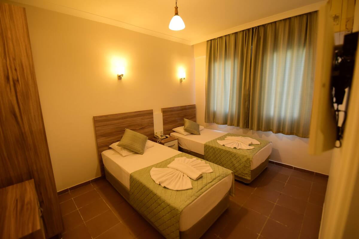 Ein Hotelzimmer mit zwei Betten, einem Holz-Kopfteil, einem Fenster mit Vorhängen und Wandleuchten.
