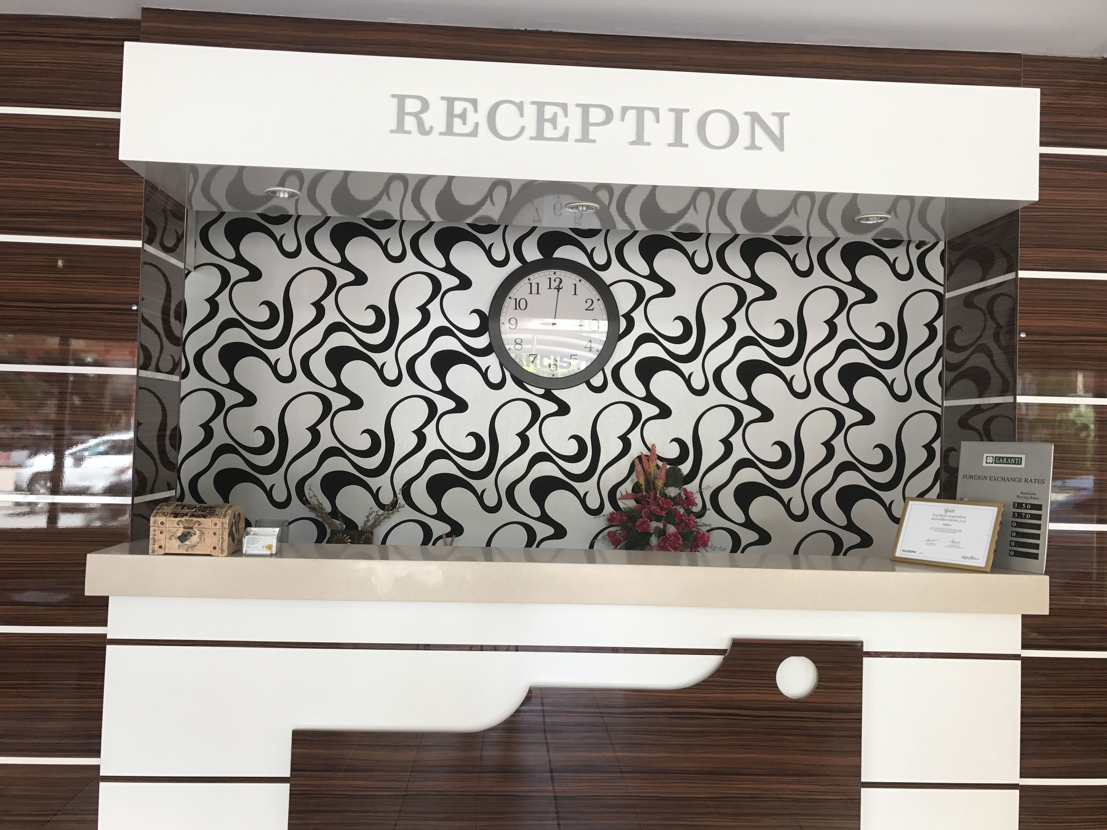 A reception desk with a 'RECEPTION' sign, a clock, and a 'FOREIGN EXCHANGE RATES' sign.