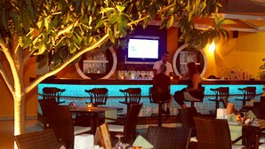 An outdoor bar area with wicker chairs and tables, a television screen, and a bar stocked with bottles. - Narcis Apart Hotel (Alanya)