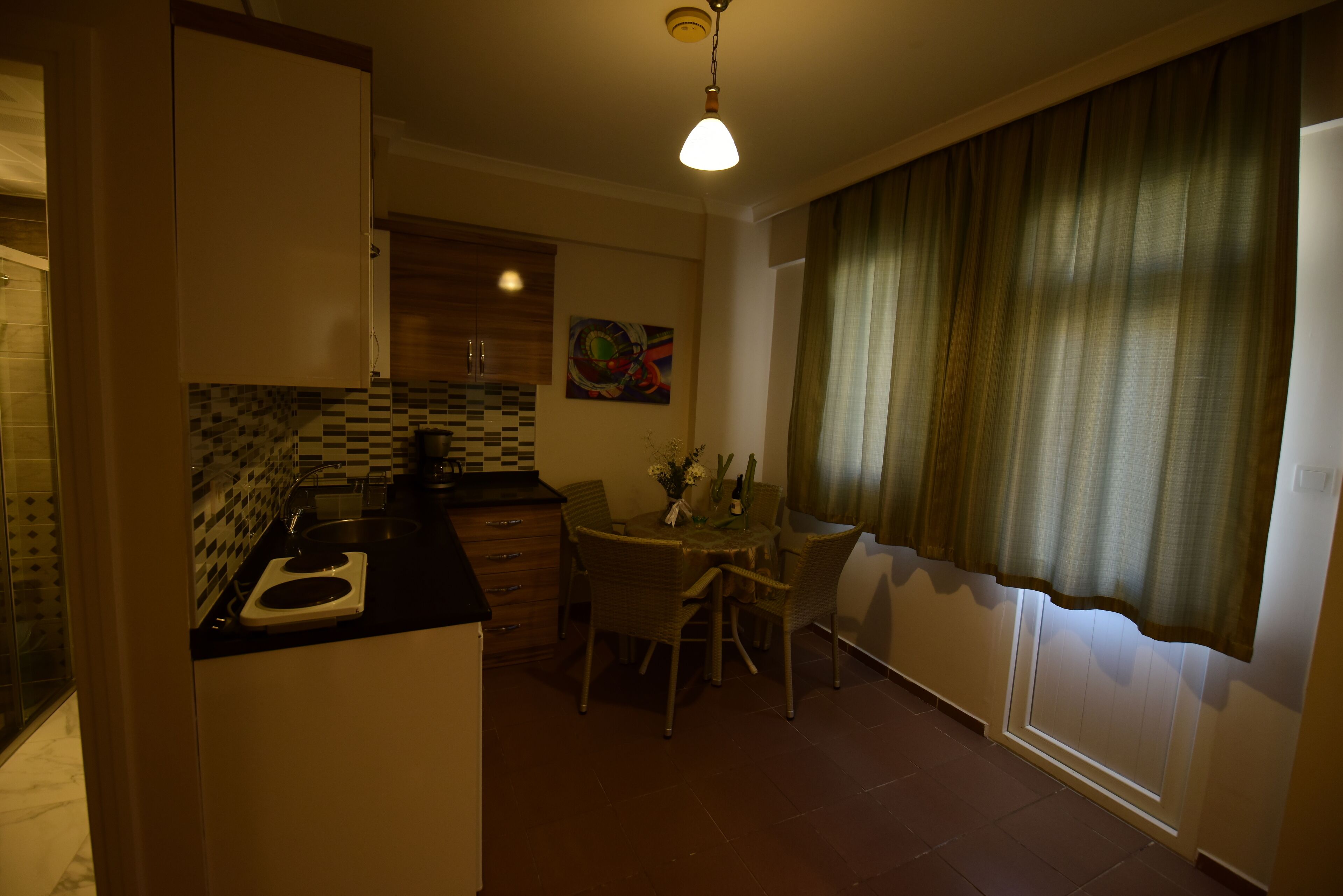 A compact kitchen with a dining area, featuring a tiled backsplash, a small dining table with chairs, and a window with curtains.