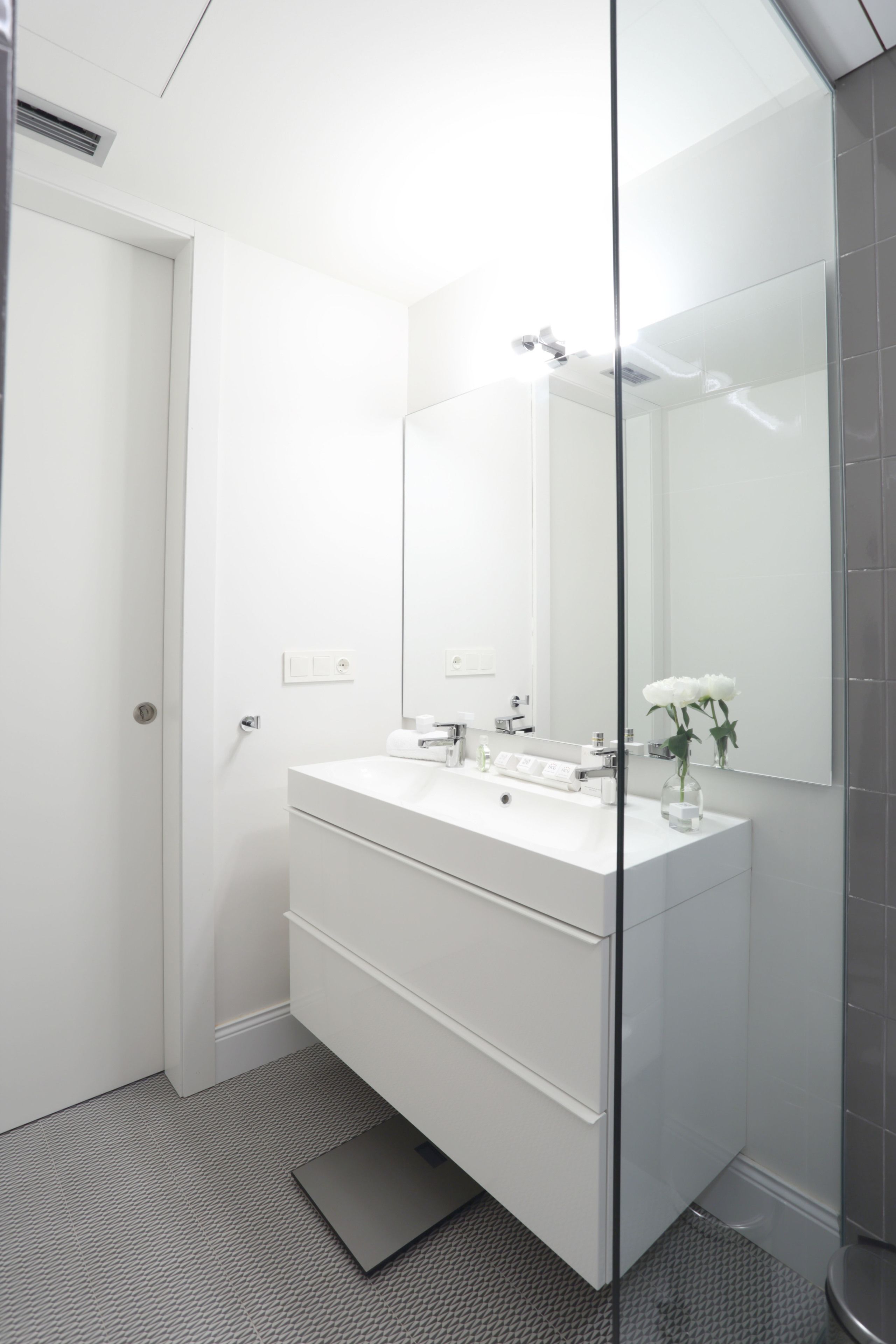 Un baño moderno con tocador blanco, un espejo grande y una cabina de ducha de vidrio.